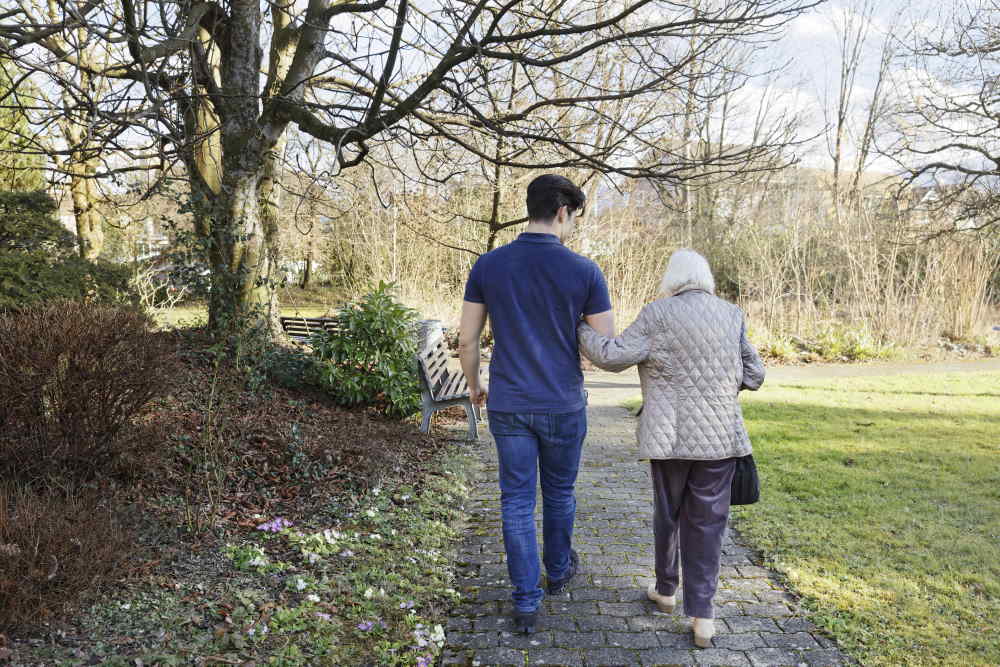 Un ragazzo sta portando a passeggiare una signora anziana.