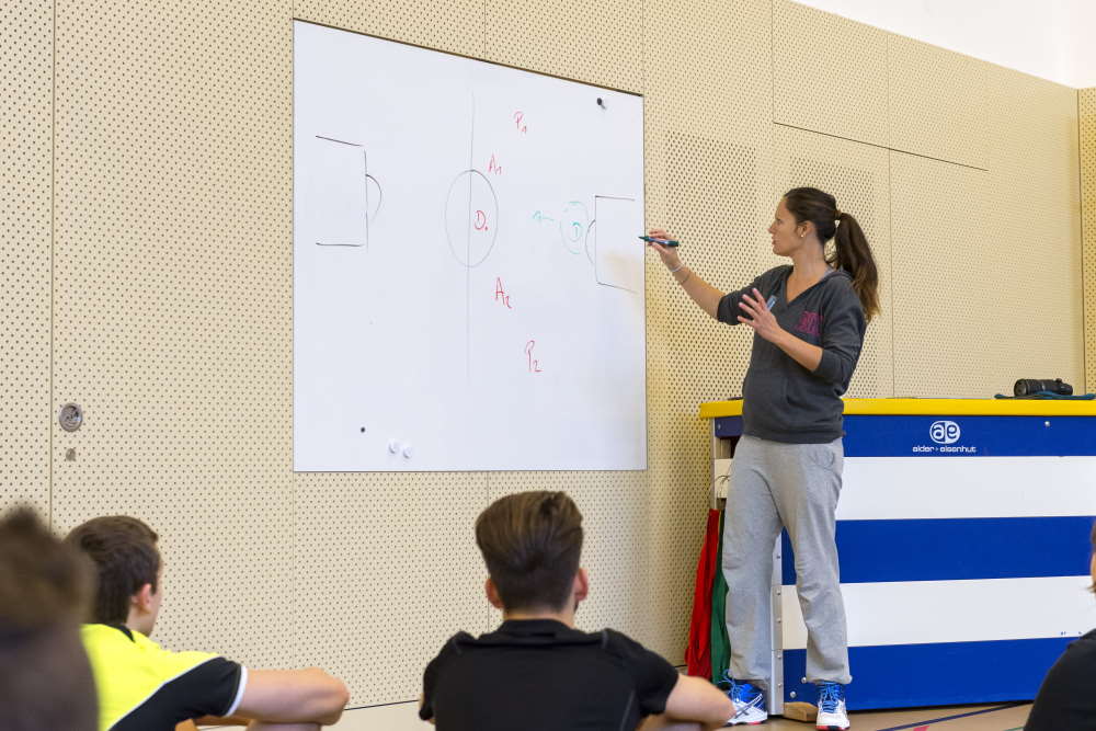 Un'insegnante di sport spiega alla lavagna uno schema di gioco.