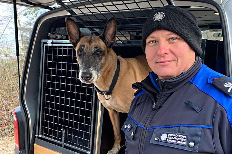 Un uomo con l'uniforme dell'Ufficio federale della dogana e della sicurezza confini sta accanto a Dynamo, cane della dogana.