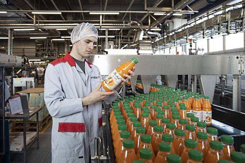 Un uomo si trova davanti a una linea di produzione di bottiglie di succo di frutta.