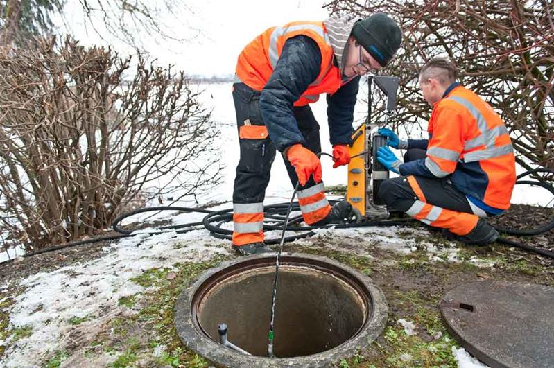 Due apprendisti controllano una canalizzazione a bordo strada.