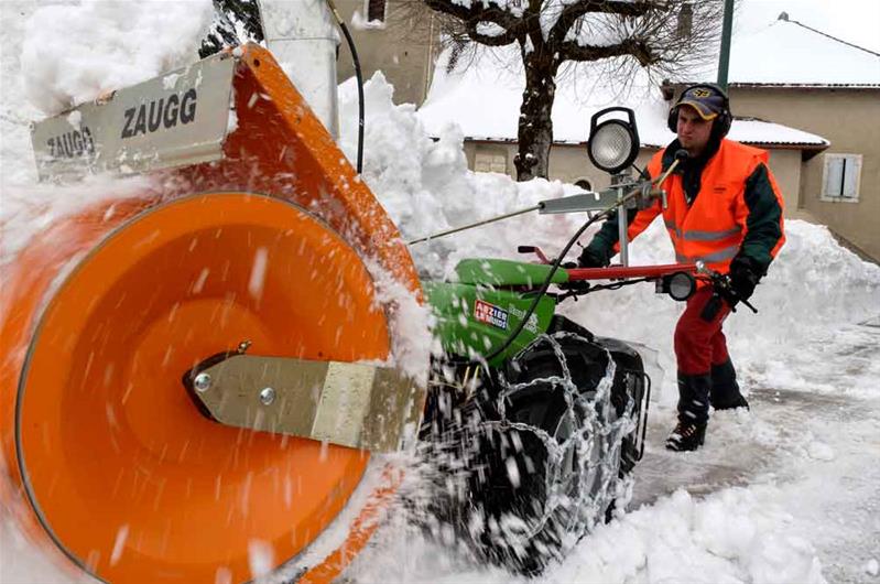 Un apprendista spala la neve dalla strada con un macchinario.