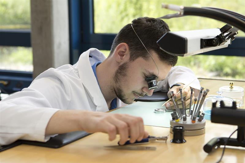 Un giovane uomo guarda un piccolo orologio con una lente d'ingrandimento.