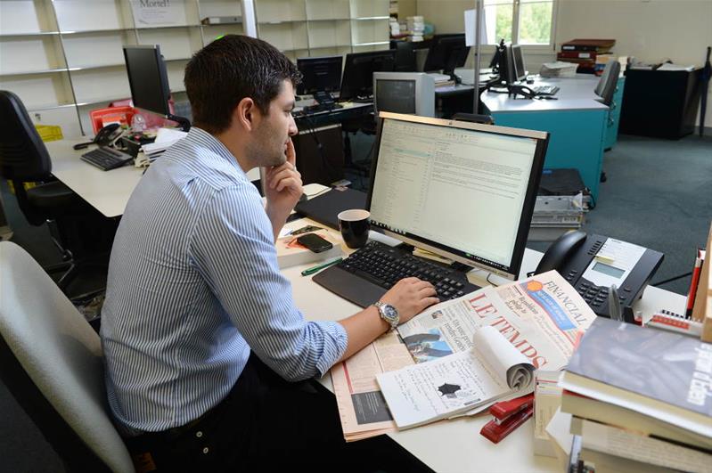 Un uomo si trova davanti al computer e sulla sua scrivania si trovano dei giornali.