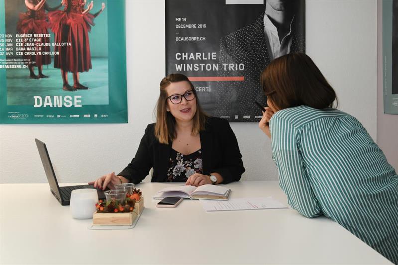 Due donne sedute a un tavolo parlano tra loro.