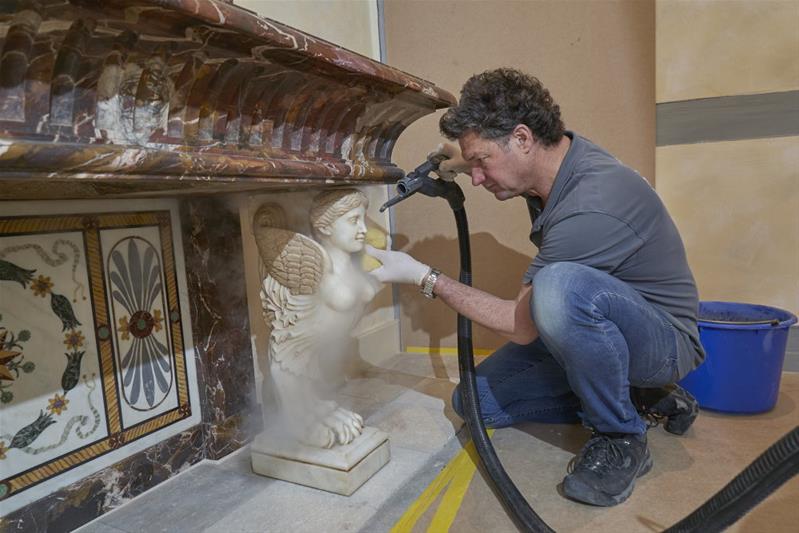 Il conservatore-restauratore pulisce la superficie di una scultura con una spugna.