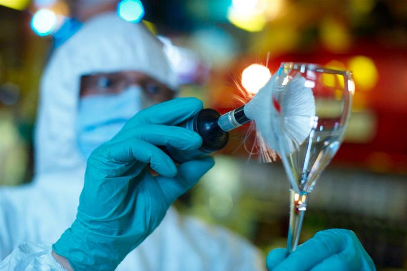 Uno scienziato che esamina un bicchiere con un pennellino per rilevare tracce