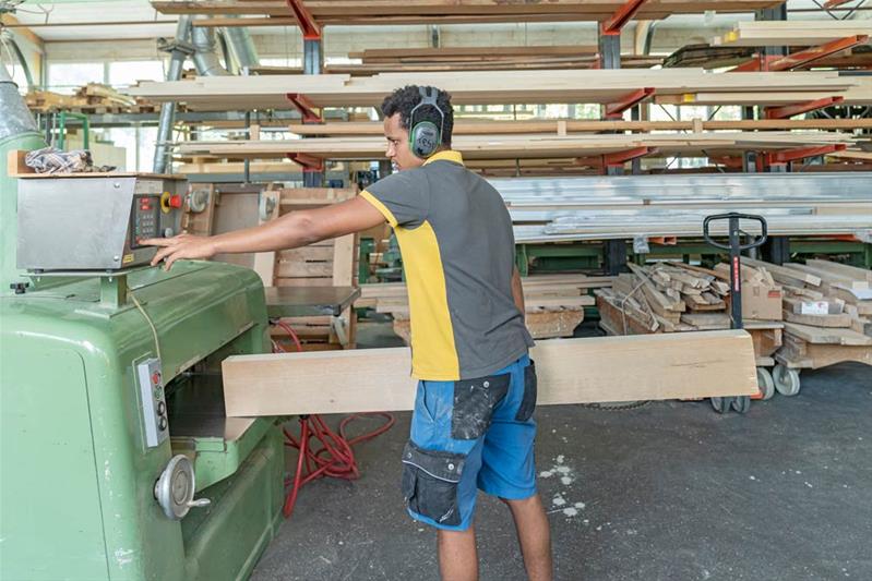 Un apprendista taglia una trave di legno con un macchinario.