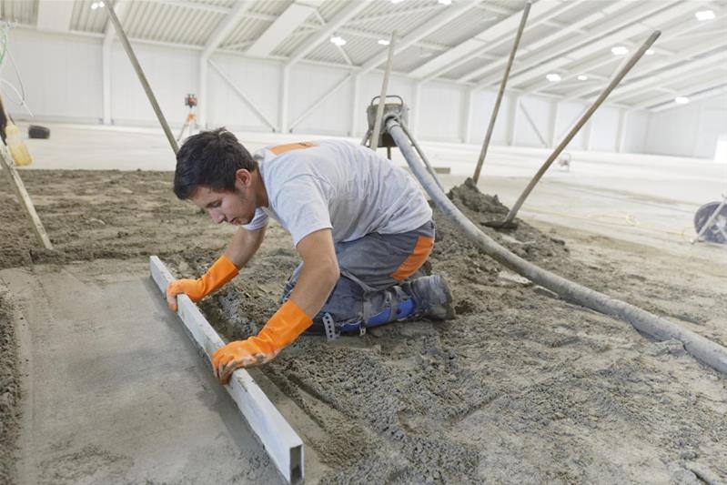 Un apprendista appiattisce e prepara il suolo per posare un rivestimento.