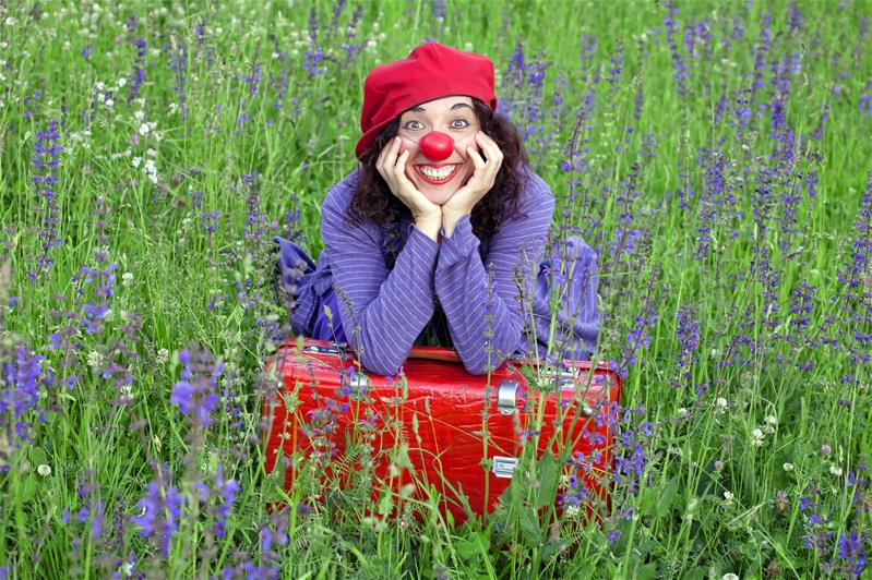 Orit Guttman sorride in un prato con la sua valigia da clown.